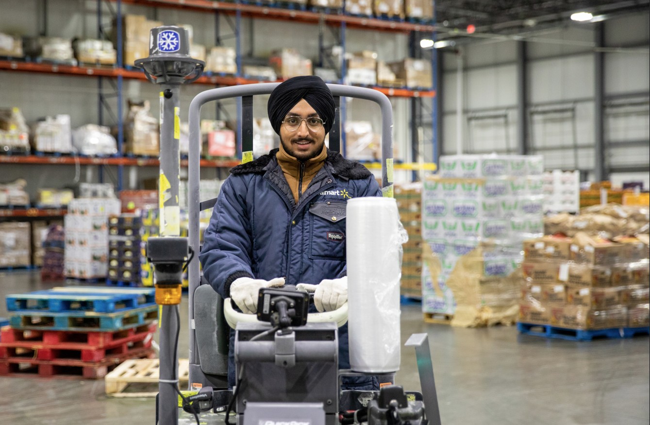 A proud Walmart truck driver smiles at the camera while standing in front of his rig.